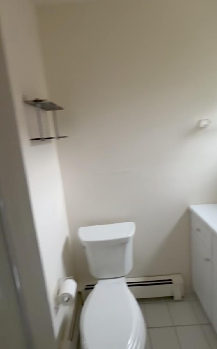 Plain white bathroom before renovation with baseboard heater