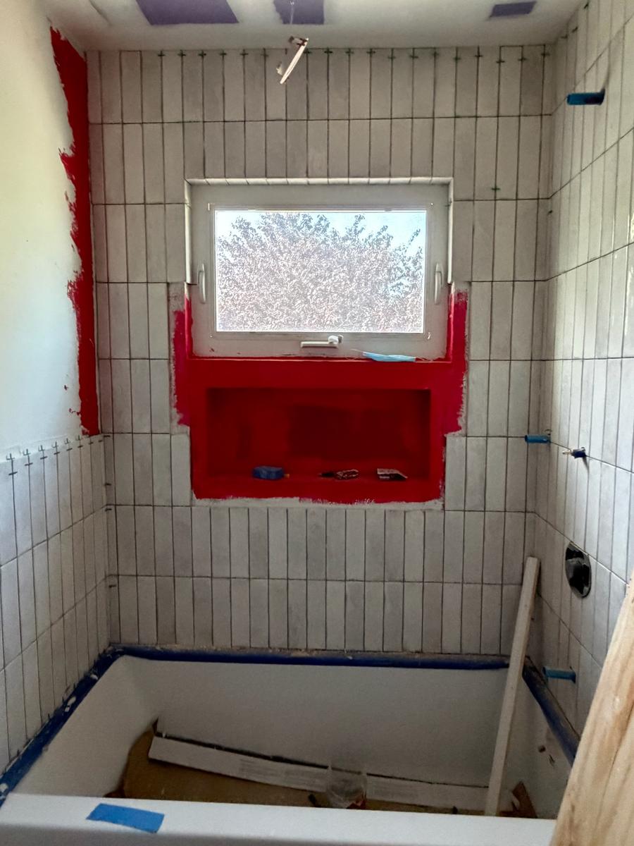 Vertical subway tile with red waterproofing membrane around shower niche