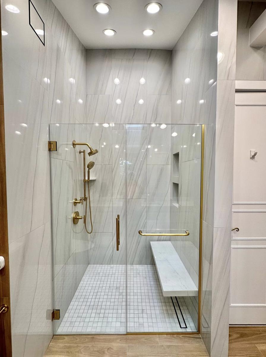 Frameless glass walk-in shower with marble walls and rainfall showerhead in luxury bathroom renovation