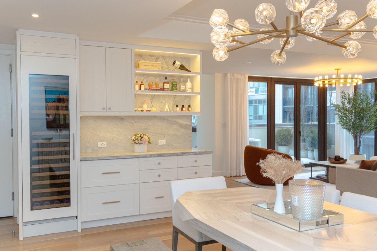 Built-in bar with a glass-front wine column, lit shelving and stone counter next to the dining table