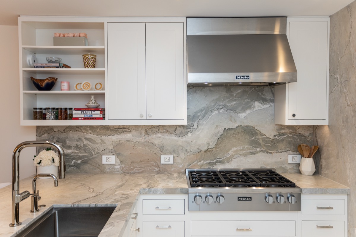 Professional range under a stainless hood with a full-height stone slab backsplash and open shelving