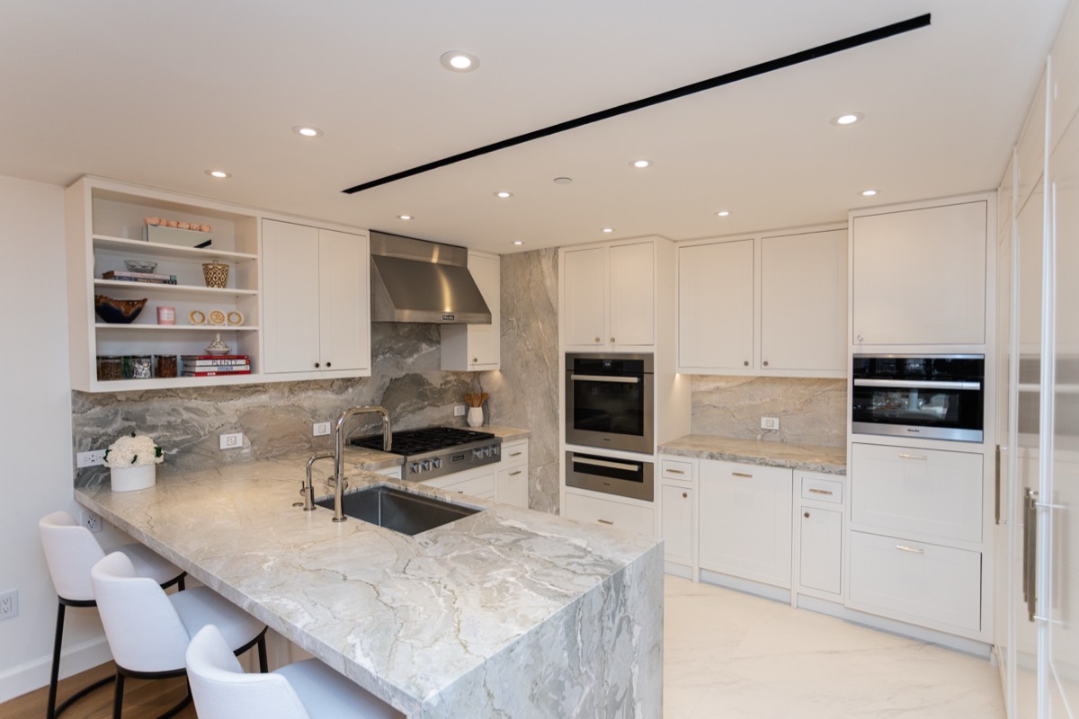 White kitchen with a marble waterfall island, counter seating, linear ceiling diffuser and built-in wall ovens