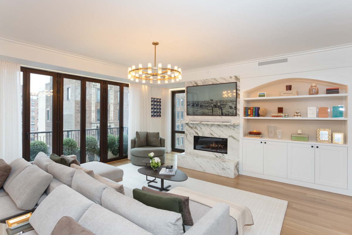 Living room in an Upper West Side five-bedroom renovation with a marble fireplace wall, arched built-in shelving and folding glass doors to the terrace