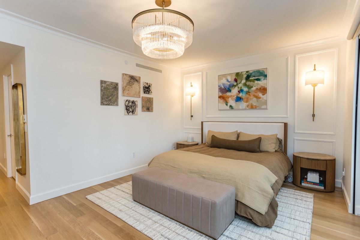 Primary bedroom with wall paneling, brass sconces and a crystal chandelier