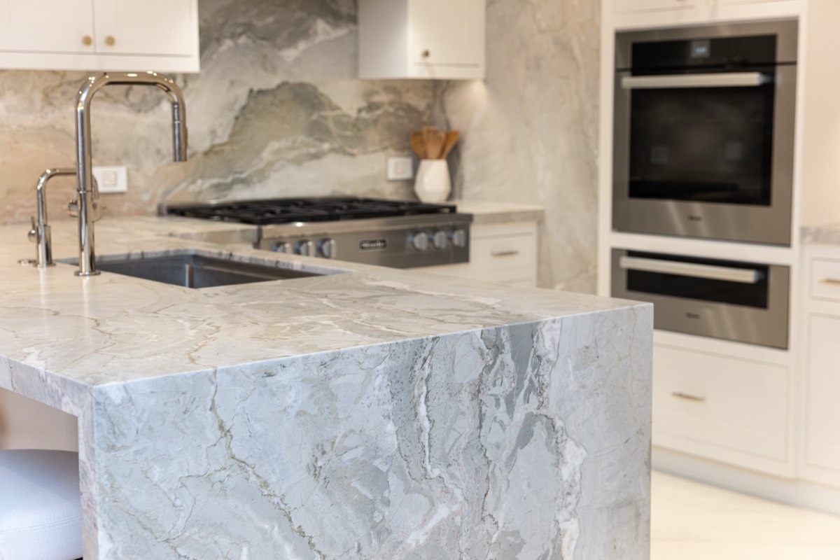 Close-up of the marble waterfall island edge, undermount sink and wall ovens